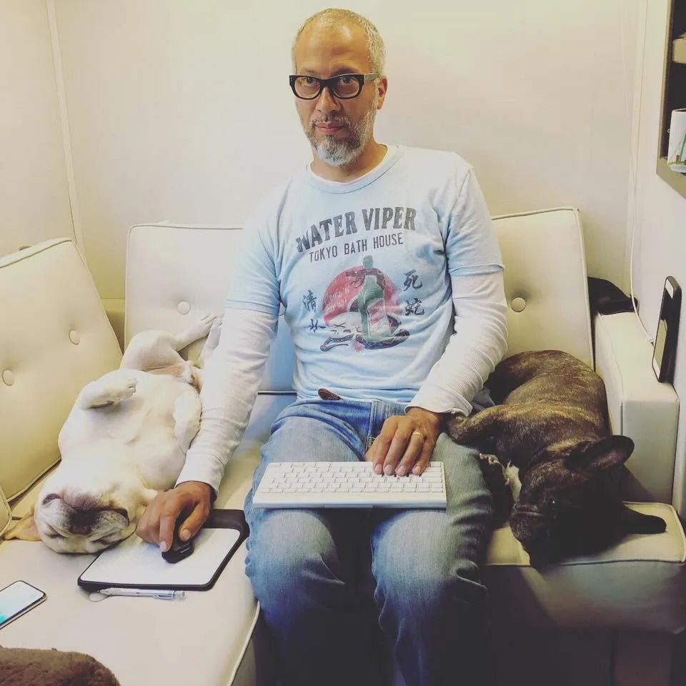 Tony working at a keyboard on the couch inside the RV, Matsu asleep on his back to the left and Porco asleep to the right